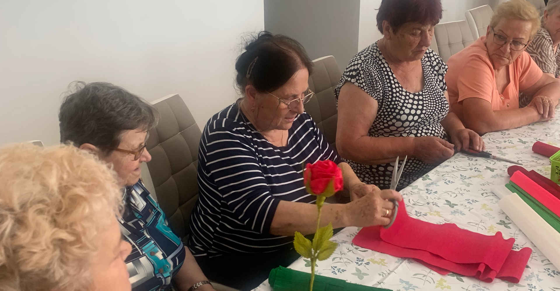 Pani Wanda szkoli seniorów w układaniu róż z krepiny